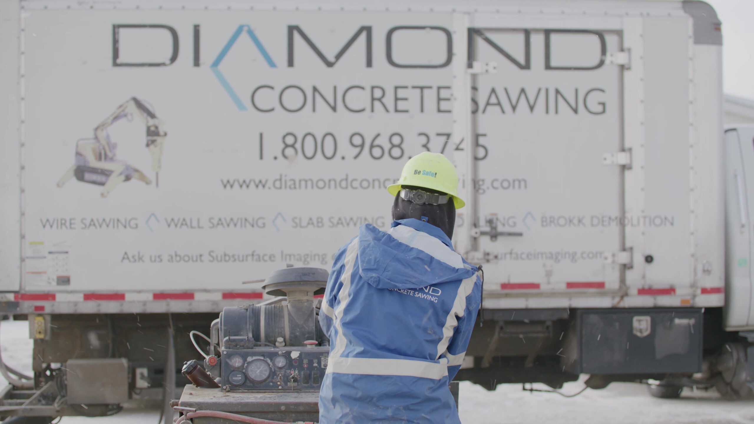 Worker in safety gear in front of a truck with 'Diamond Concrete Sawing' branding.